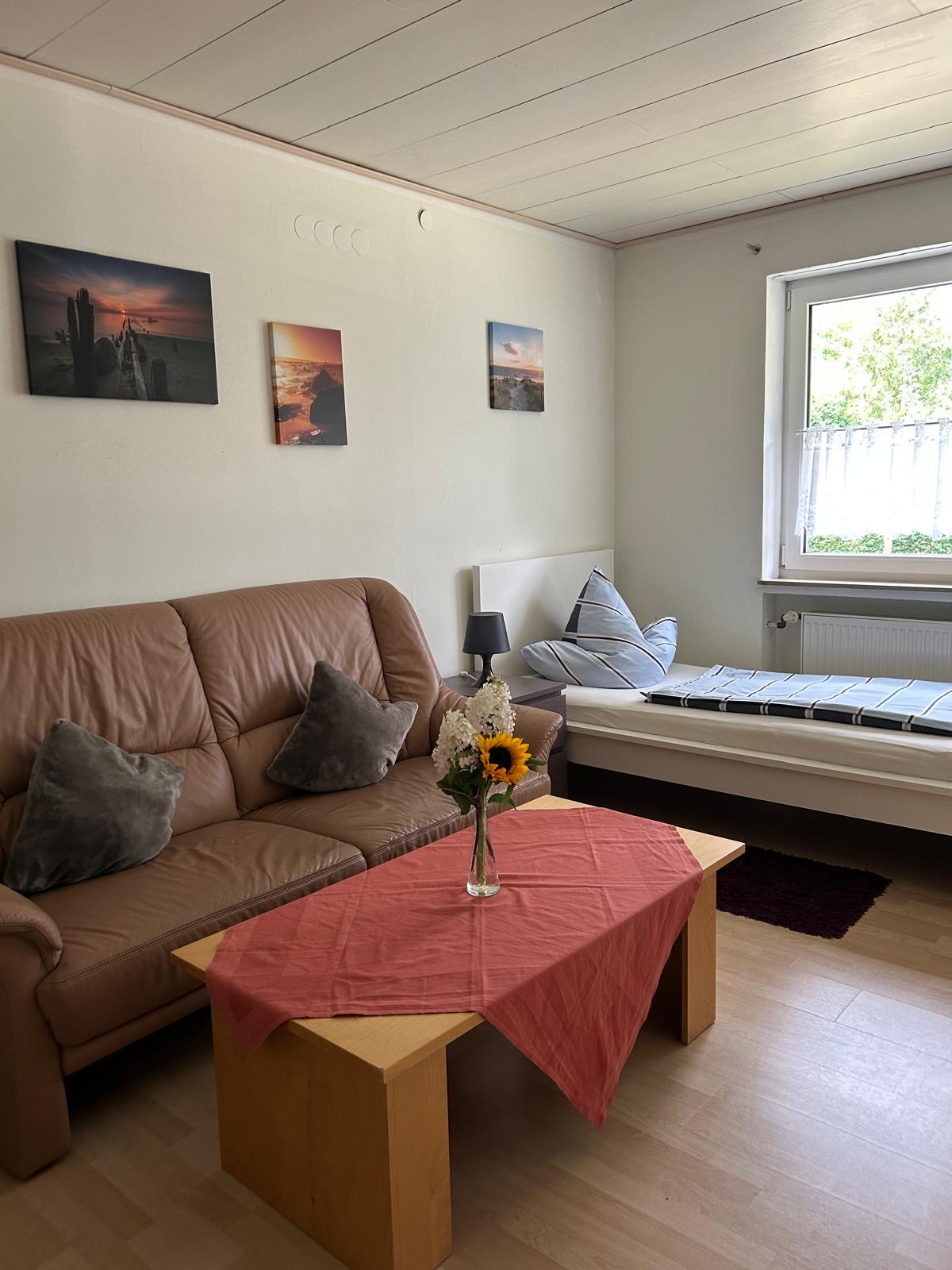 Wohnbereich mit Ledersofa, Bett und Strandbildern – Monteurzimmer Donauwörth